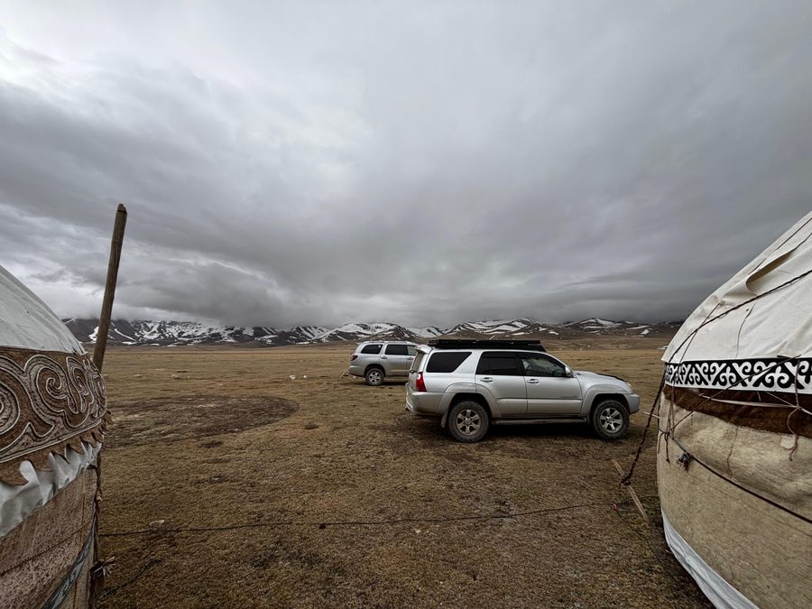 Two 4×4 vehicles between yurts under stormy alpine sky