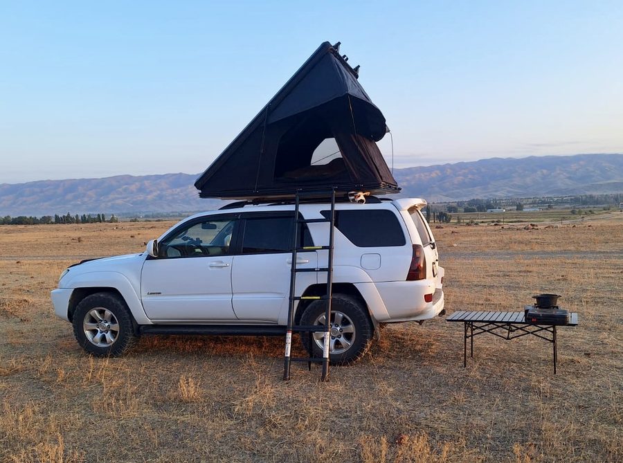 White 4×4 with rooftop tent on a golden Kyrgyz plain at sunset