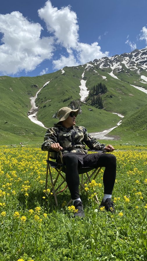 Camp chair in a yellow wildflower meadow under snow-capped Tien Shan peaks